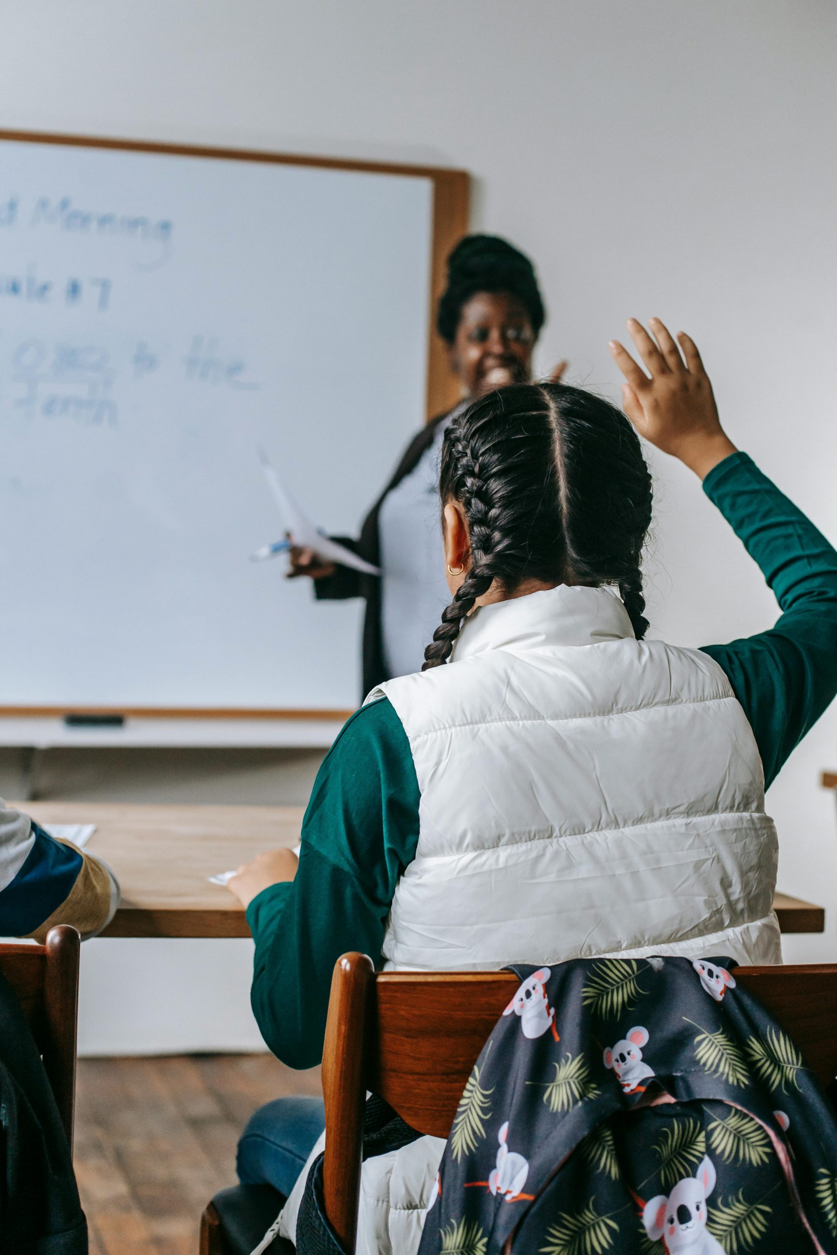 Child raising hand in class, empowered to achieve dreams.